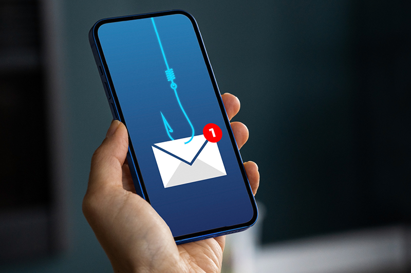 Person holding a mobile phone which is displaying an icon of an envelop being caught with a fish hook and fishing line, representing email scams and phishing