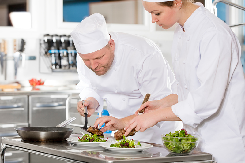 Two chefs in uniform, preparing meals in a restaurant kitchen