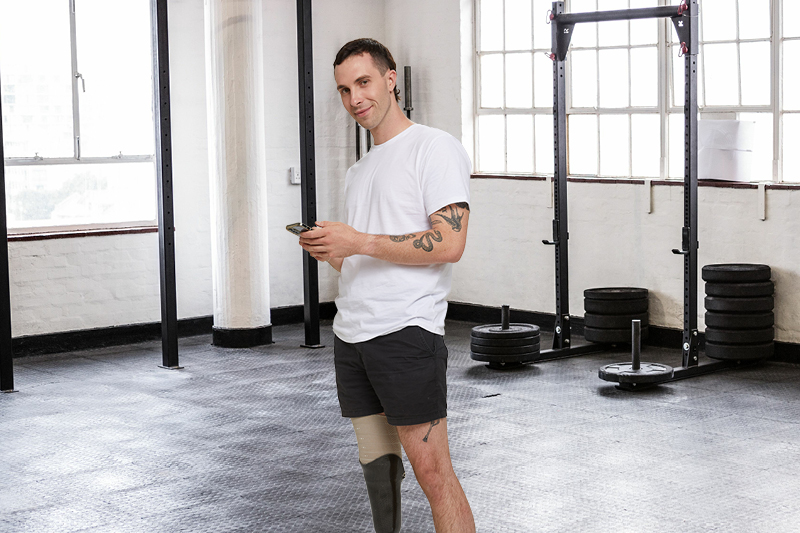 A young person in activewear with a prosthetic leg in a gym using their smart phone